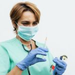 Nurse preparing a syringe for vaccination, wearing a face mask and gloves.
