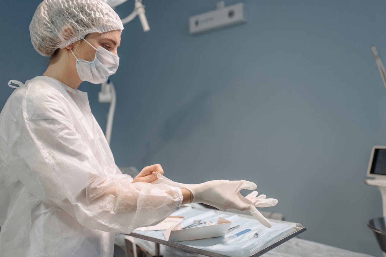 A female medical professional dons protective gloves in a sterile operating room setting.